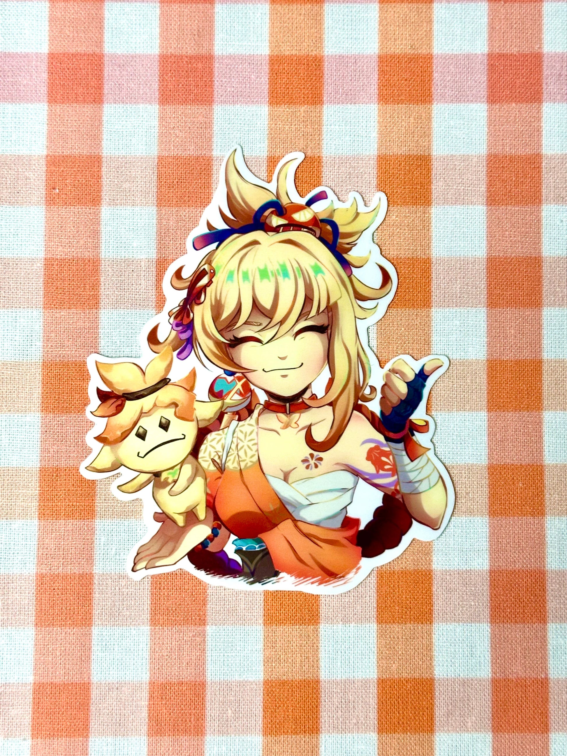 A die-cut sticker of Yoimiya, a character from the game Genshin Impact, seated with a small statue, with a white border and glossy finish on an orange checkered background.